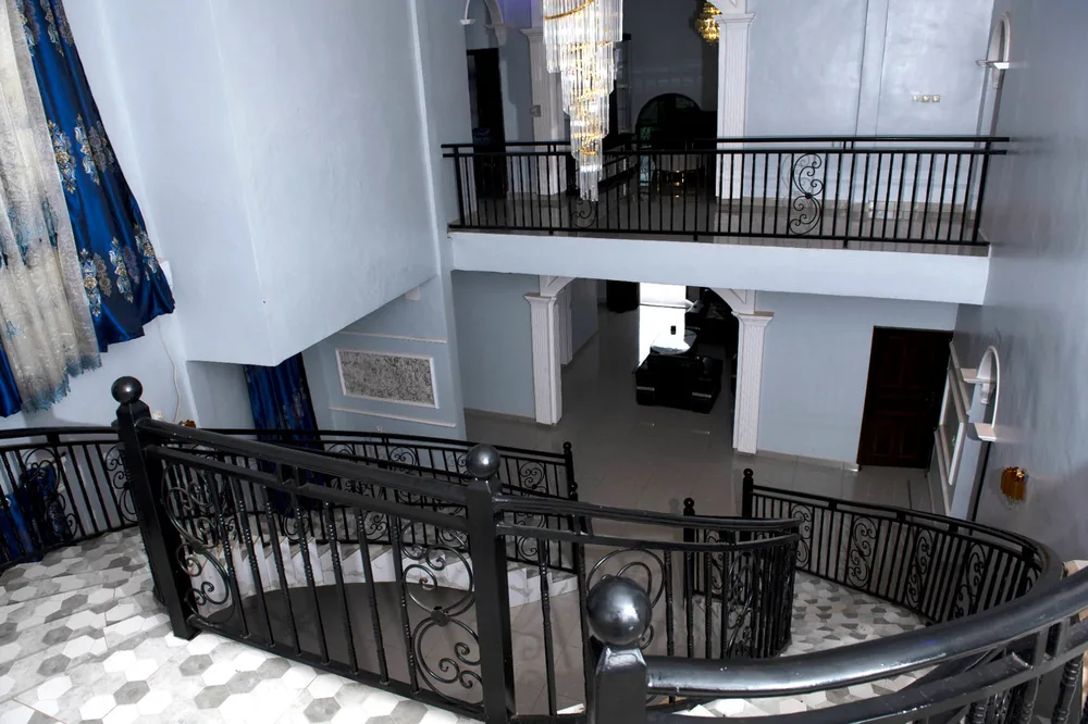 Interior staircase at Celebrity Guest House with black wrought-iron railings, chandelier and tiled floor